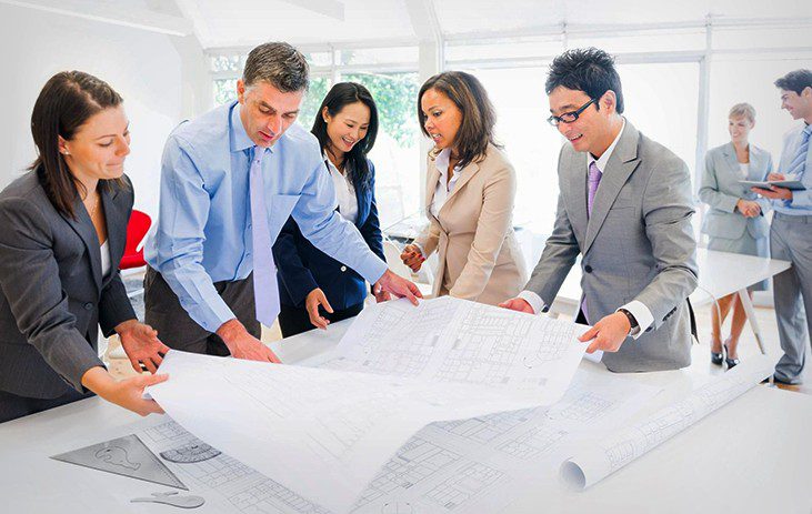 A group of people in business attire looking at plans.